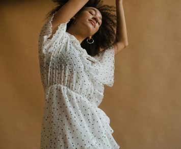 pexels-photo-5885751-5885751 Joyful woman with curly hair dances gracefully in a white dress indoors.